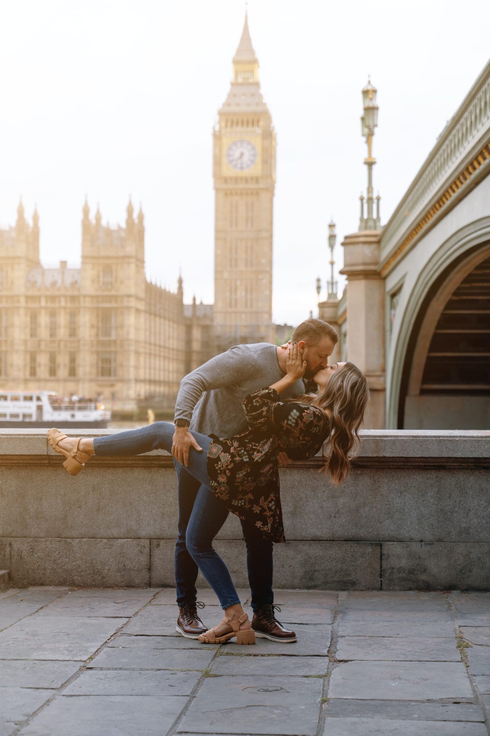 a man and woman kissing in front of a clock tower